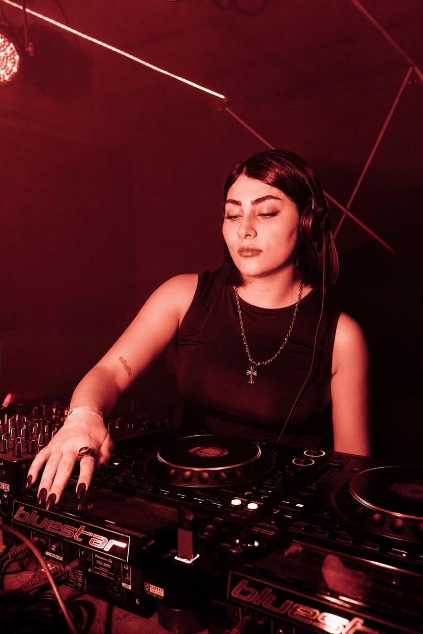 5OGOL at CDJs under a red lamp, hands on the jog wheel